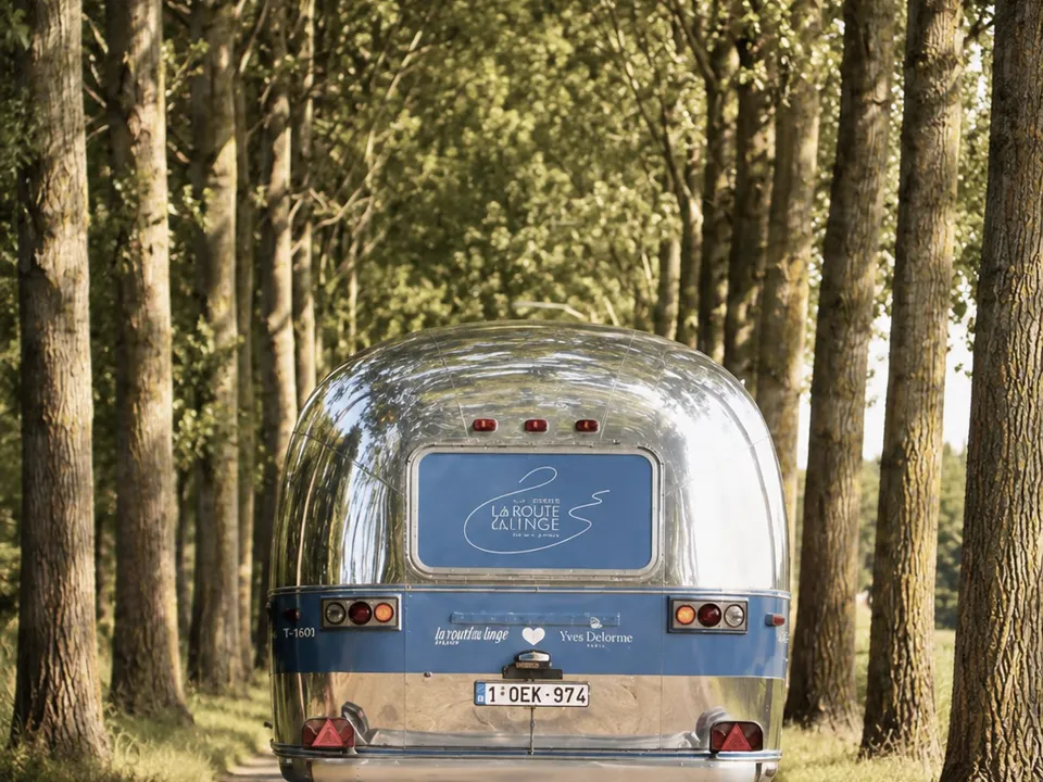 Caravane Airstream habillée sur une route de campagne bordée de peupliers