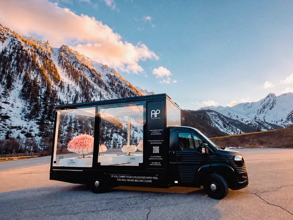 Camion vitrine noir AP Collection stationné sur une route de montagne enneigée au soleil couchant
