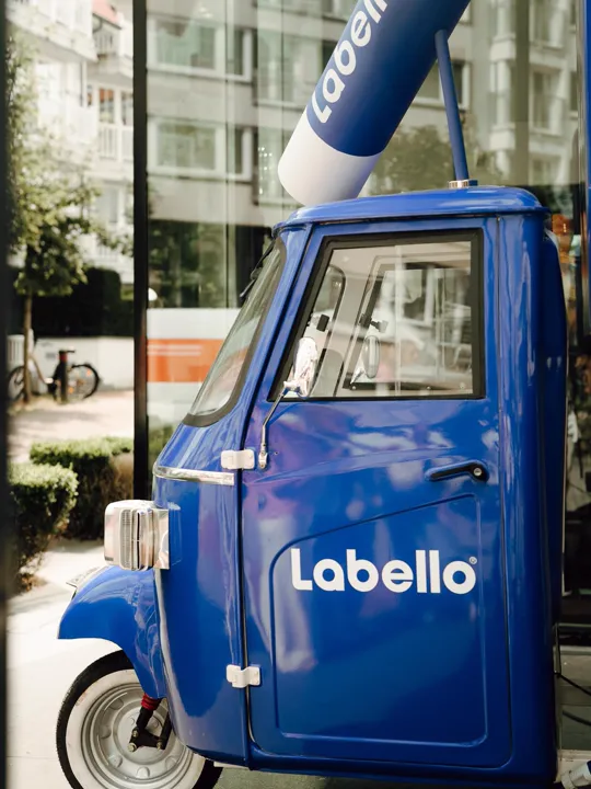 Triporteur bleu habillé Labello, tube géant sur le toit, vue de face en ville
