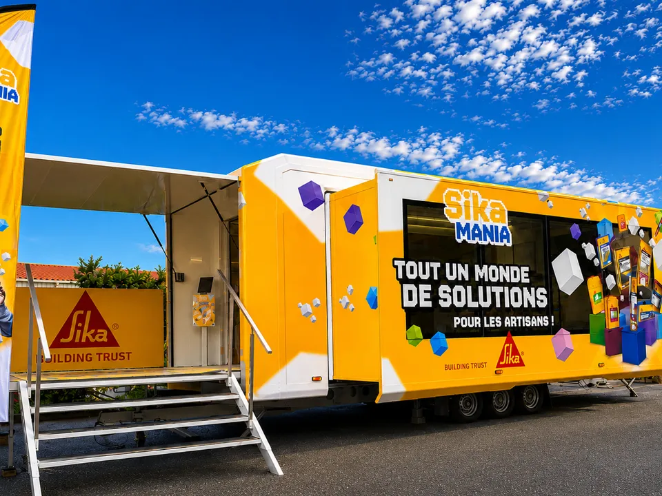 Camion podium orange Sika Mania déployé sur une pelouse, beach flags et escalier d'accès