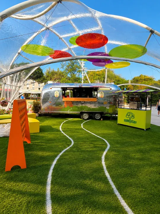 Caravane Airstream sous un dôme transparent à disques de couleur, comptoir vert de la marque sur la pelouse